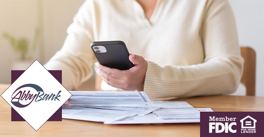 woman looking at mobile phone and paper bills