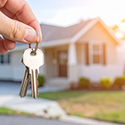 hand holding keys up in front of small modular home blurred in the background