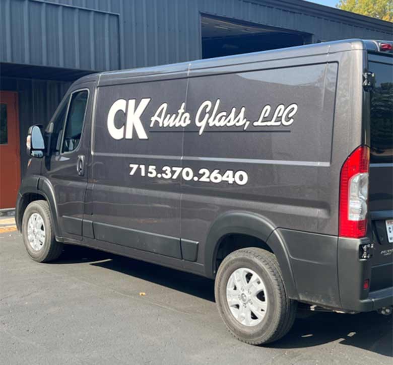 view from the back driver side of a large black van with the words CK Auto Glass and their number on the side