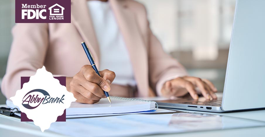 business woman writing in notebook while working on laptop