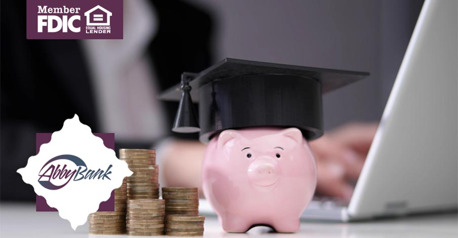 piggy bank with graduation cap and stack of coins with person on laptop in background