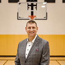 Brian Butch in suit smiling on basketball court with hoop in background