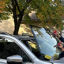 close up of a new windshield carefully being placed in a vehicle outside