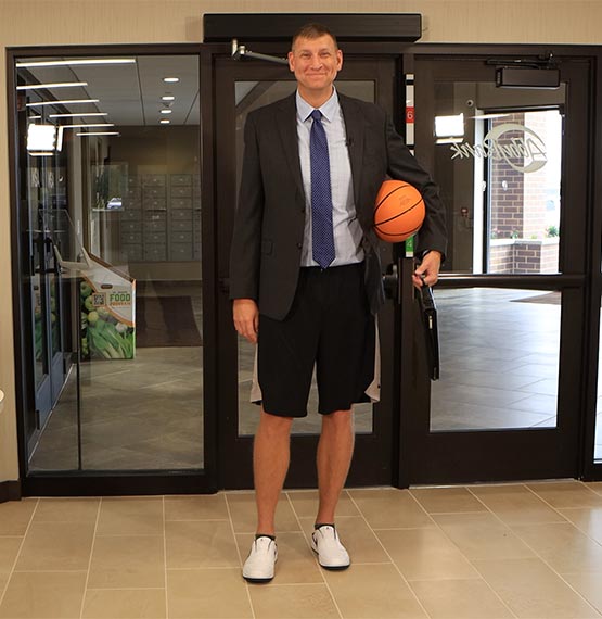 Brian Butch walking into AbbyBank carrying a basketball under one arm with a padfolio in his hand