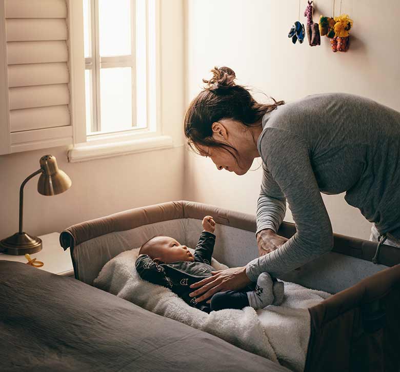 mother checking on young baby in bedside bassinet