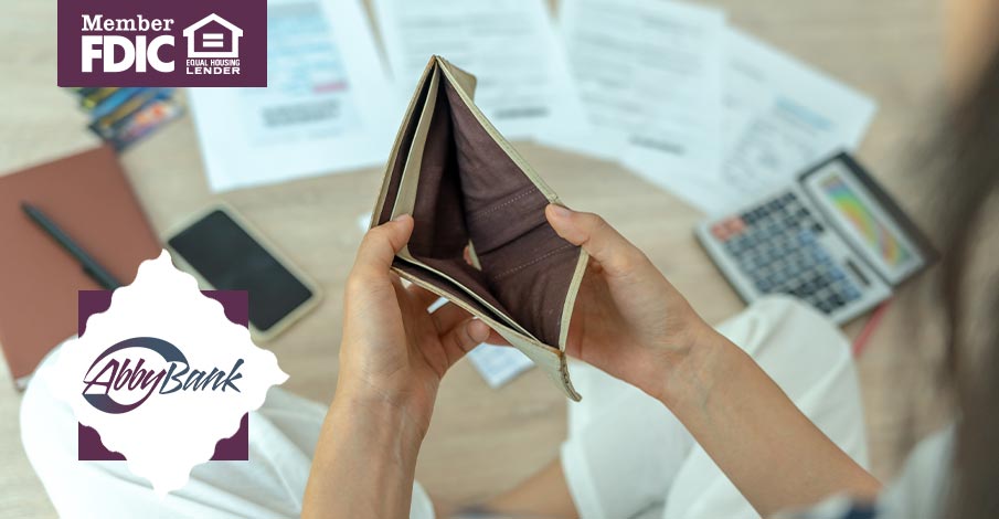 woman looking in empty wallet with calculator and papers nearby