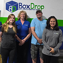 team of four posing by BoxDrop Mattress & Furniture Direct logo in Weston warehouse
