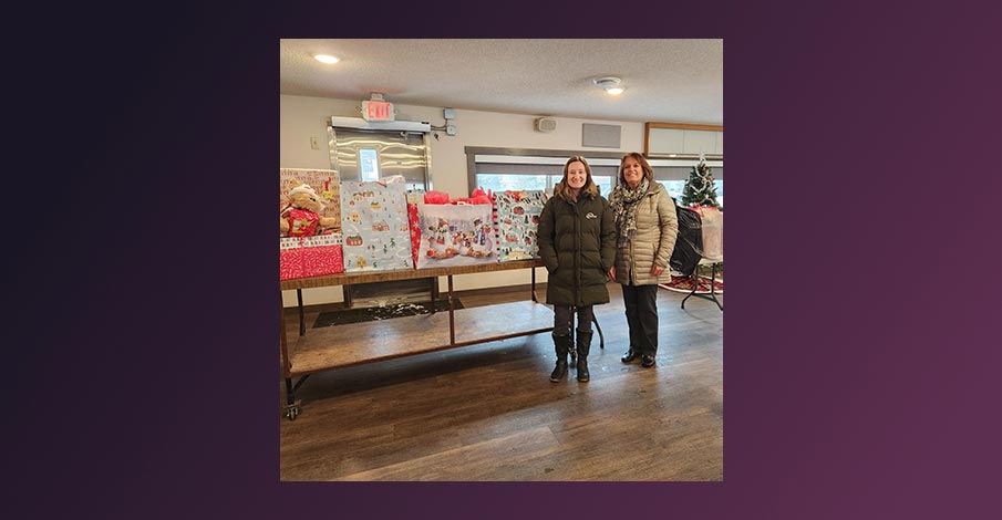 Gail, AbbyBank Marketing Assistant, and Karla, Abbotsford Branch Manager, pose in front of table full of wrapped gifts from Abbotsford Holiday Wishes Tree in 2024