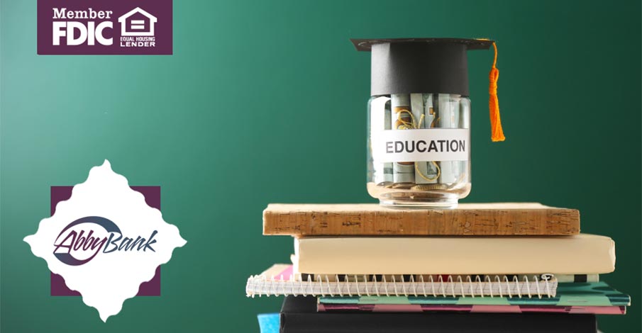 stack of textbooks and notebooks with graduation cap jar full of money sitting on top